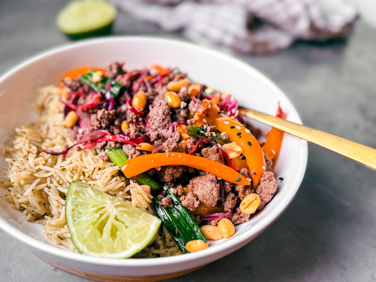 Close up of bowl of ground beef stir fry over rice with a lime wedge.