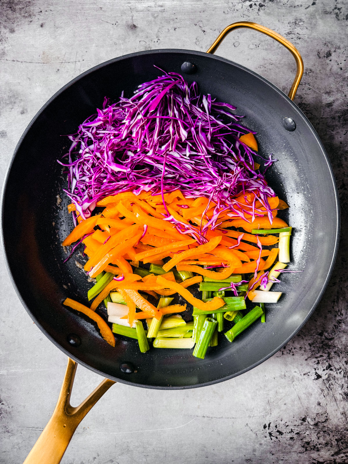 Pan with shredded red cabbage, orange bell pepper, and chopped scallions.