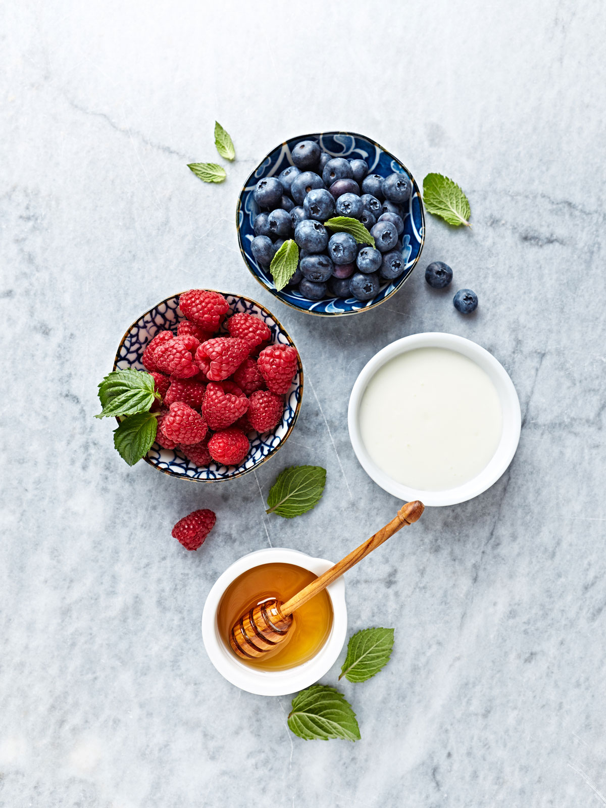 Bowls of raspberries and blueberries next to cream and honey.