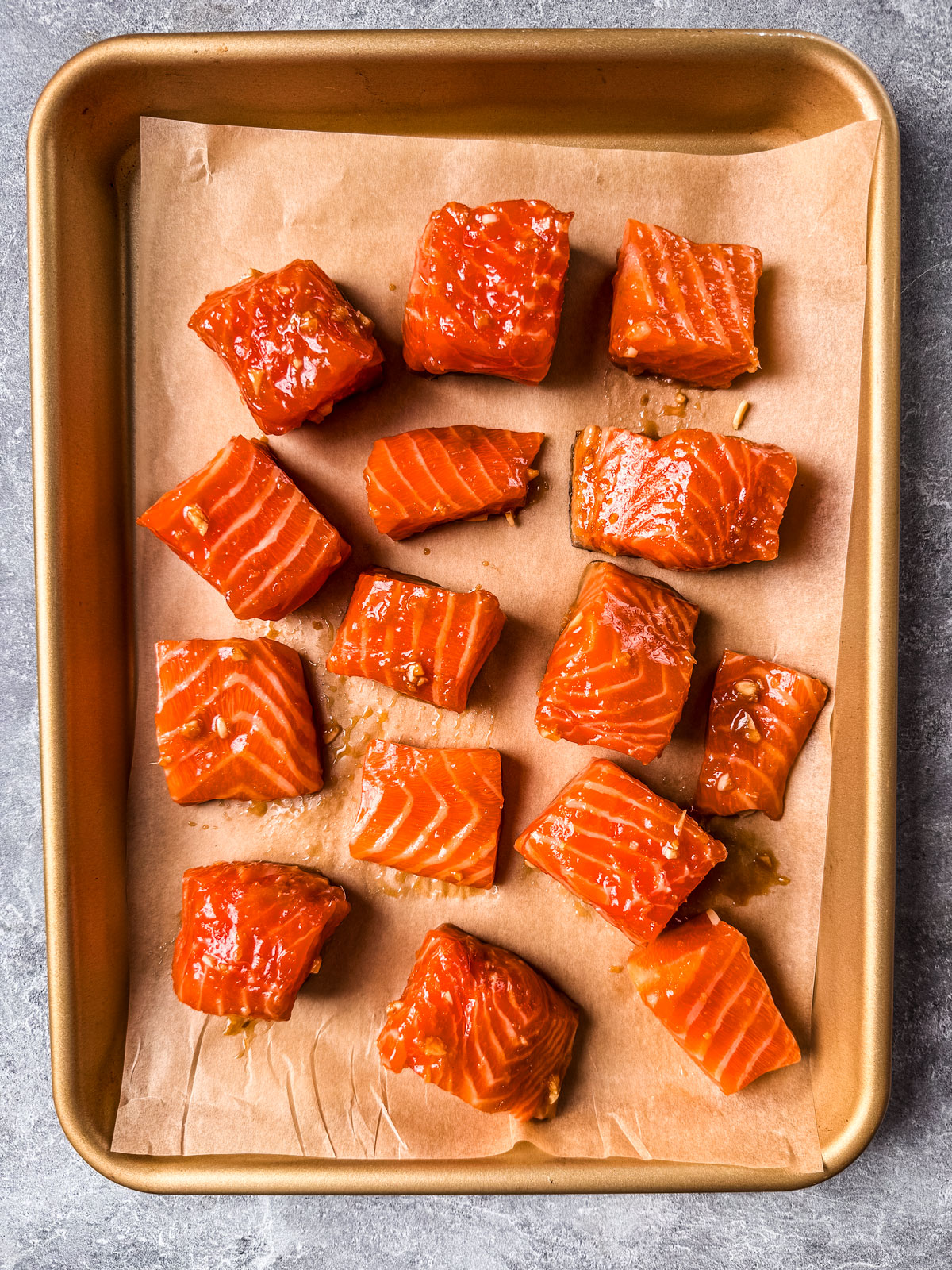 Marinated salmon cubes on a parchment-lined baking sheet.