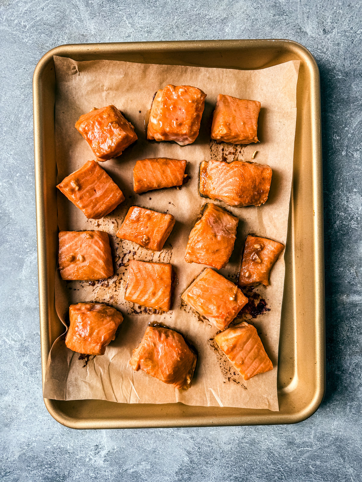 Cooked cubed salmon on parchment-lined baking sheet.