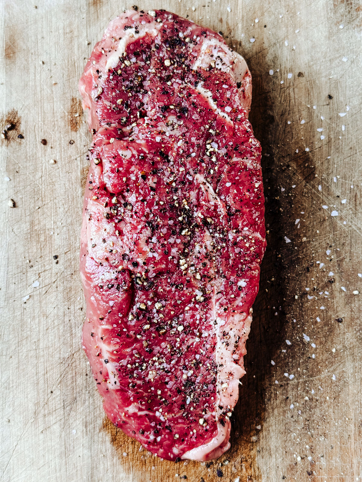 Raw steak on a cutting board seasoned with salt and pepper.