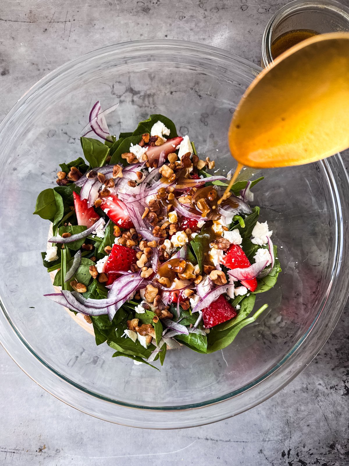 Large mixing bowl full of salad ingredients being drizzled with dressing.