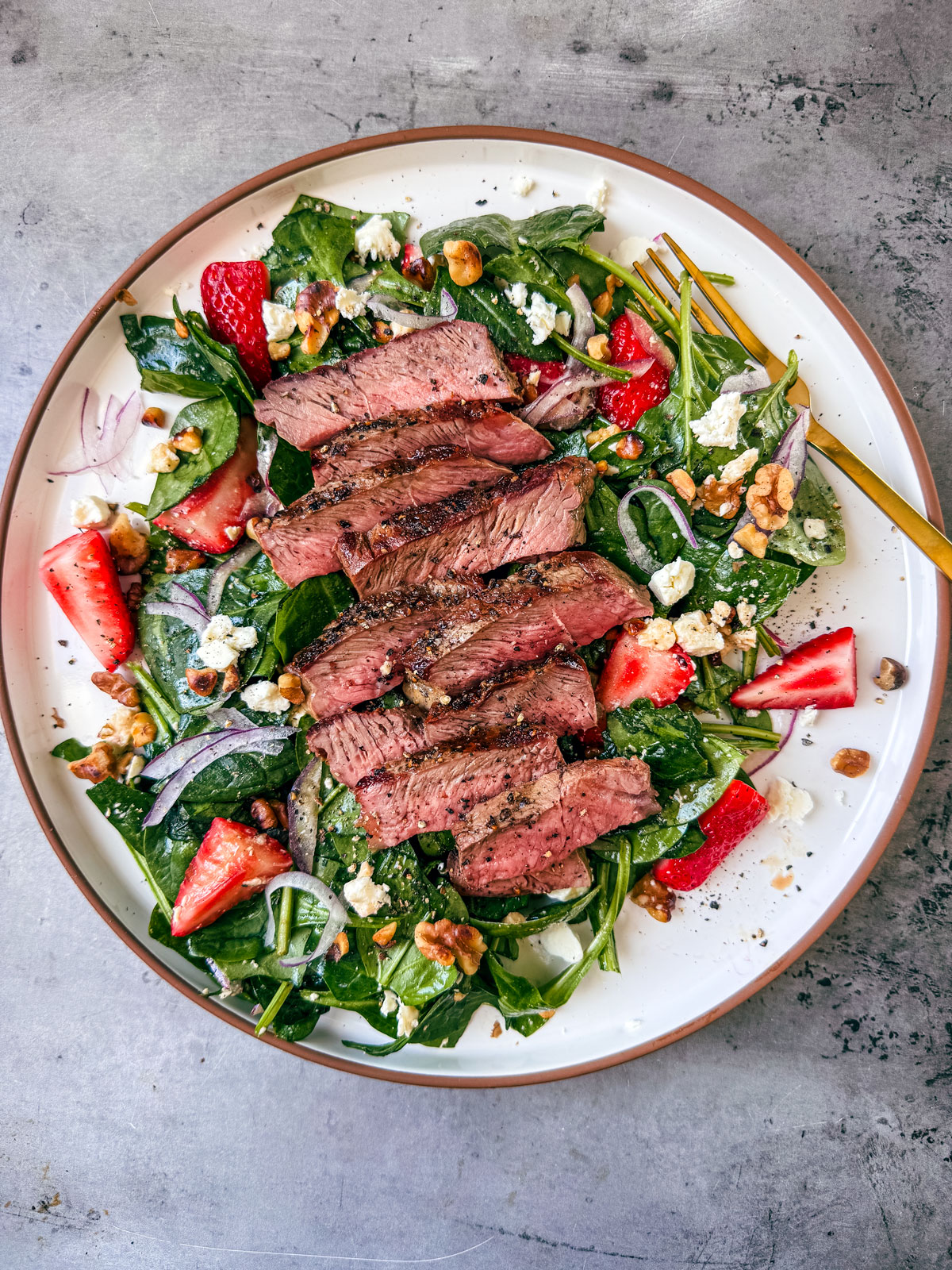 Steak slices over strawberry spinach salad on a plate.