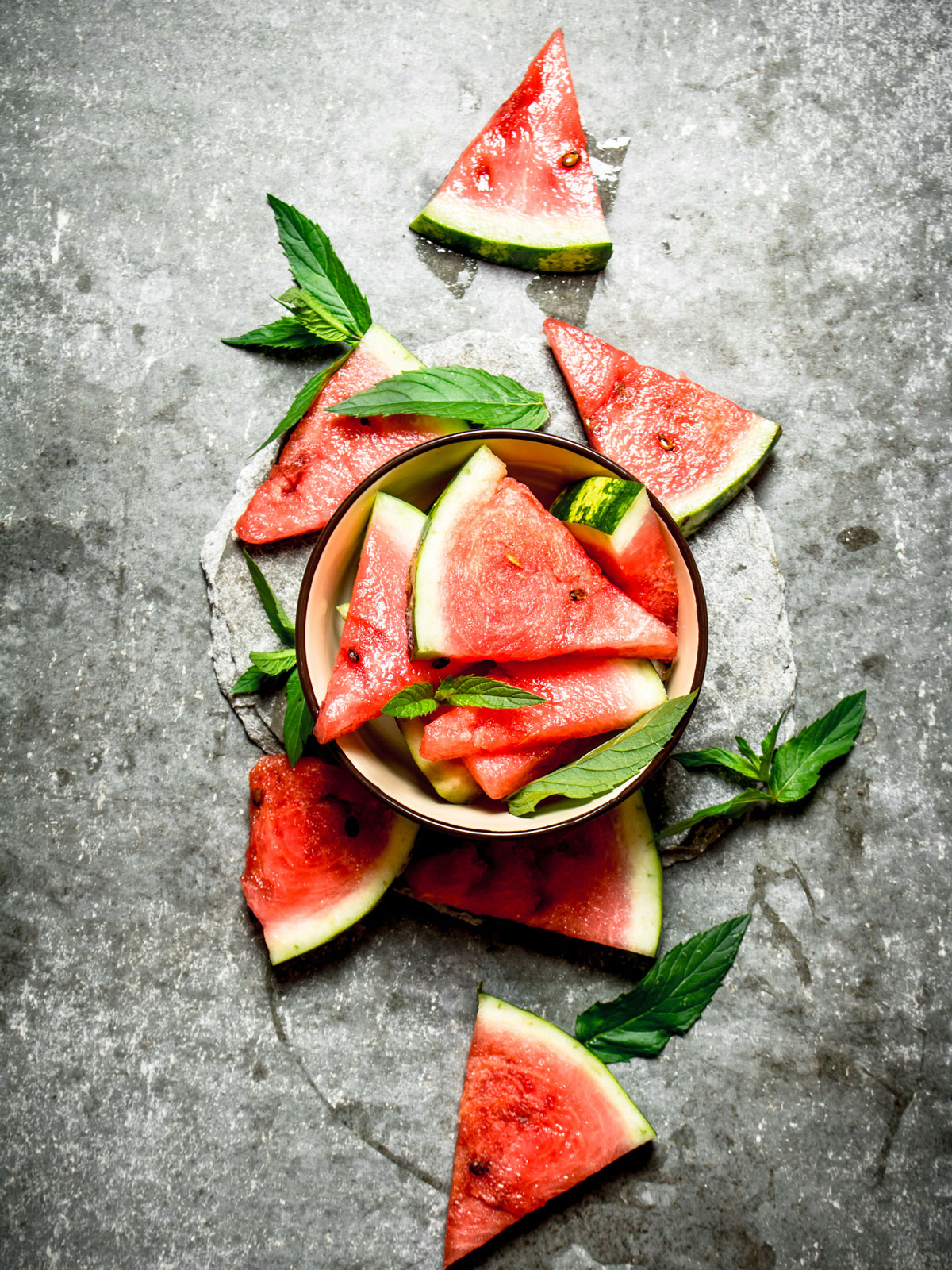 Watermelon wedges in a serving bowl and on a stone table.