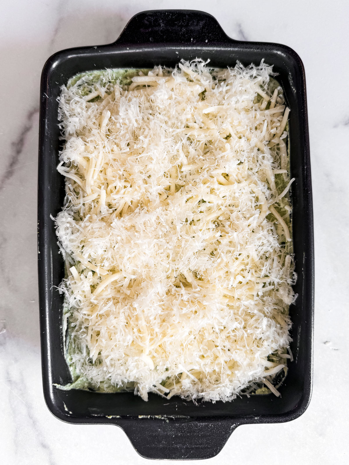 Dip mixture covered in grated mozzarella and parmesan cheese.