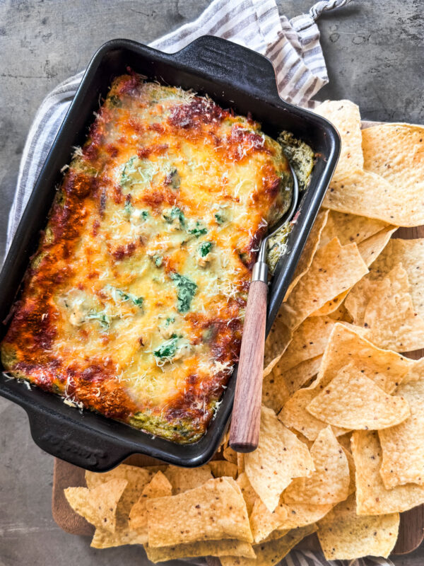 Baked spinach and artichoke cottage cheese dip in a baking dish surrounded by tortilla chips.