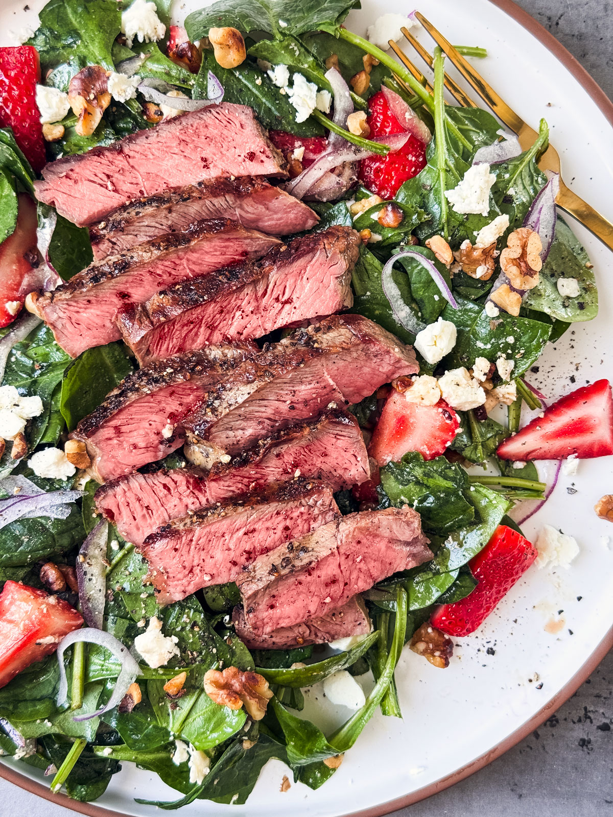 Close up of steak over spinach salad with strawberries.